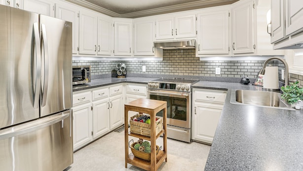 A modern kitchen with white cabinets, stainless steel appliances, a brick backsplash, and a wooden island with baskets. - Covered Patio! Modern Home in Jackson (Jackson)