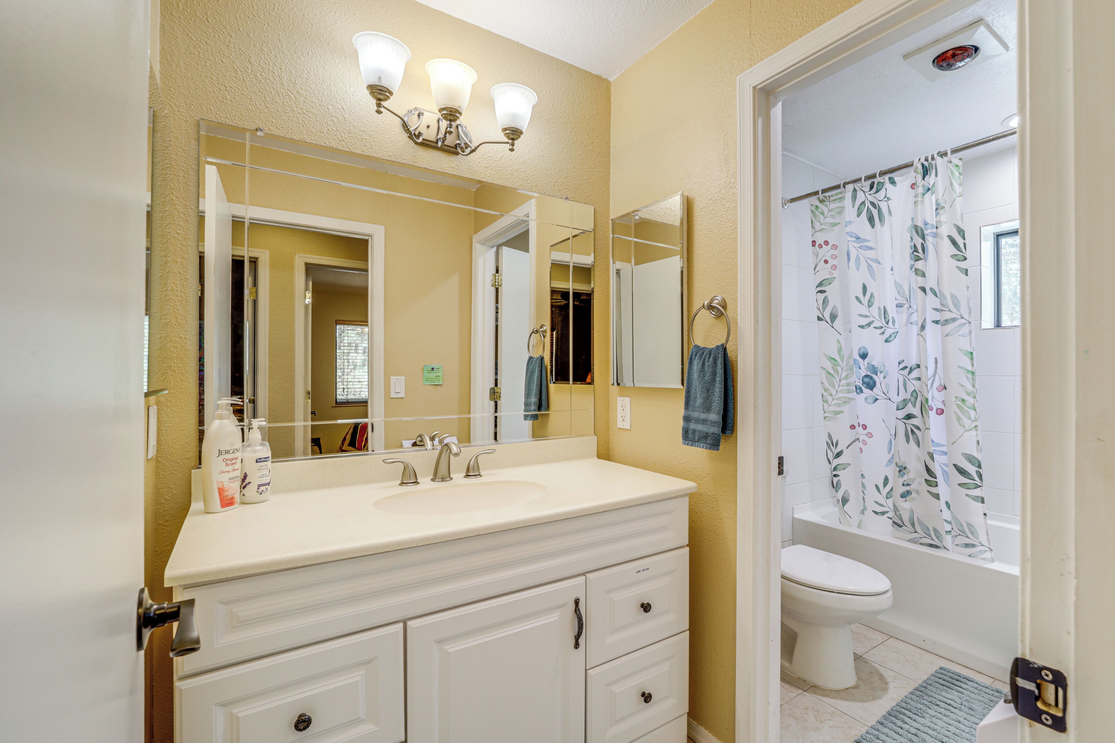 A bathroom with a white vanity, a large mirror, a shower curtain with a floral pattern, and a toilet.