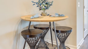 A round wooden table with a vase of flowers and two matching stools.