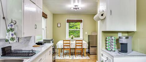 A kitchen with white cabinets, a stainless steel refrigerator, a Keurig coffee maker, and a window with a view of greenery.