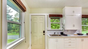 A kitchen with white cabinets, a sink, and a window with a view of greenery. - Mt Rainier Retreat 7 Mi to Park Entrance! (Ashford)
