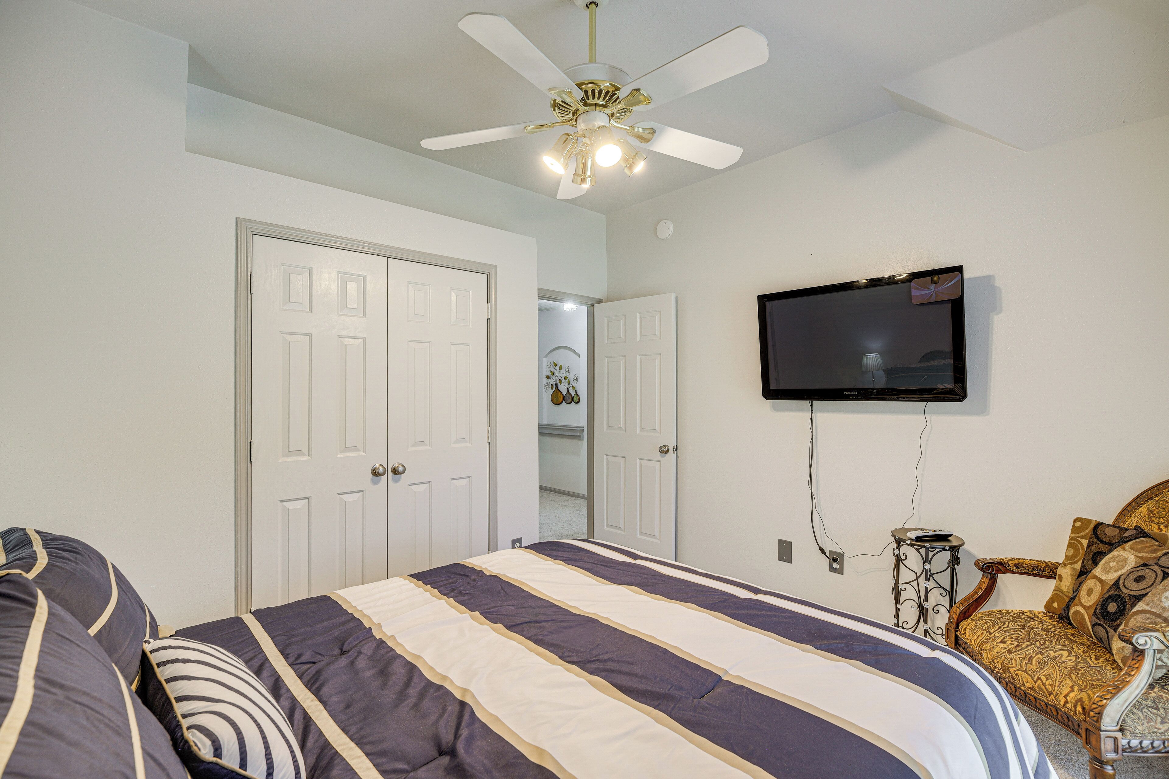 A bedroom with a bed, a ceiling fan, a TV mounted on the wall, and a chair.