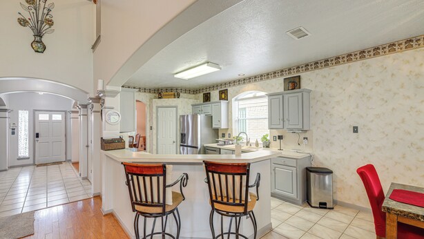 A kitchen with a central island, two bar stools, a red chair, and a trash can.
