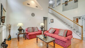 A spacious living room with two red sofas, a coffee table, and a staircase leading to an upper floor.