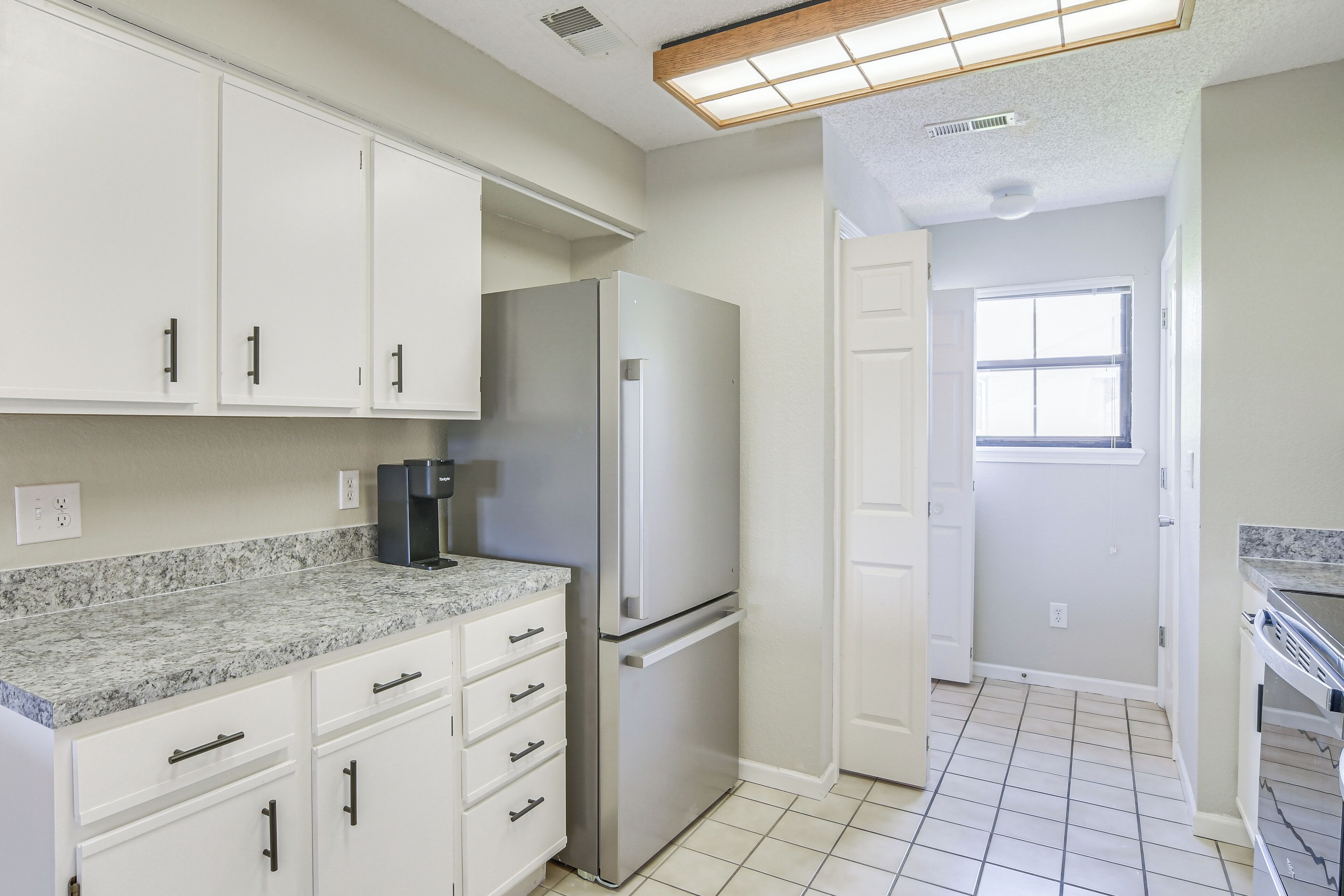 A kitchen with white cabinets, a stainless steel refrigerator, and a granite countertop.