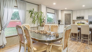 A dining area with a round table surrounded by six chairs, a kitchen with white cabinets, a microwave, and a refrigerator. - 12 Mi to Possum Kingdom Lake: Graford Getaway! (Graford)