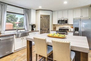 A modern kitchen with white cabinets, stainless steel appliances, and a wooden island with chairs. - 12 Mi to Possum Kingdom Lake: Graford Getaway! (Graford)