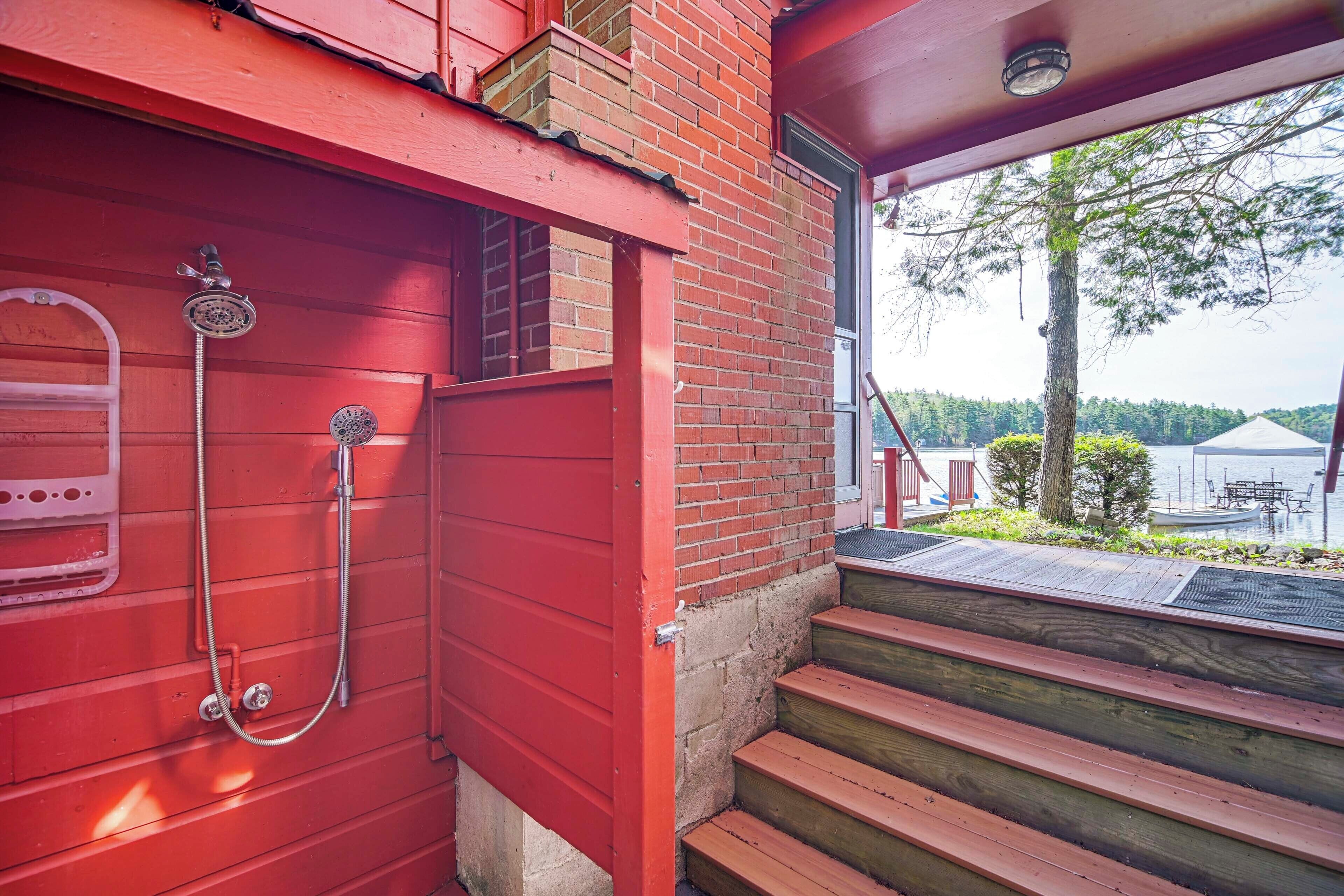 Exterior de madera roja con puerta metálica, ducha y escalera de madera que lleva a una terraza.