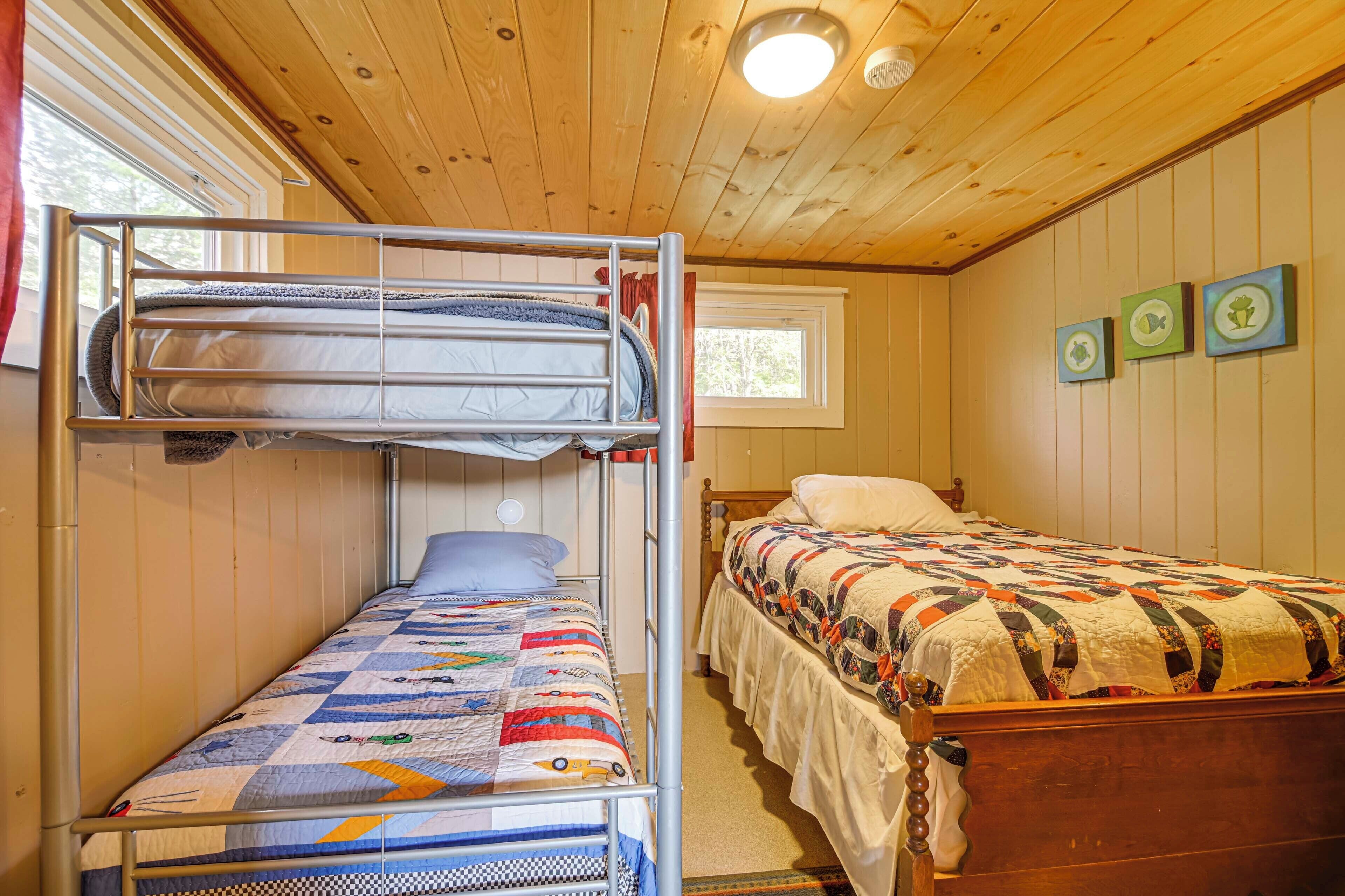 Una habitación con dos camas, una litera y una cama individual, paredes de madera y una ventana.