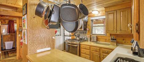 A kitchen with wooden cabinets, a stove, and hanging pots.