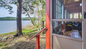 A cabin with a glass door, a wooden deck, and a view of a lake.