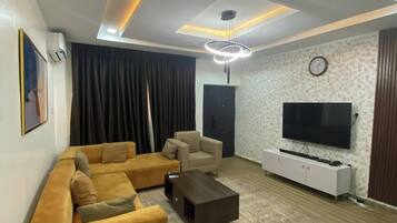 A modern living room with a sectional sofa, a coffee table, a TV, and a patterned wall.