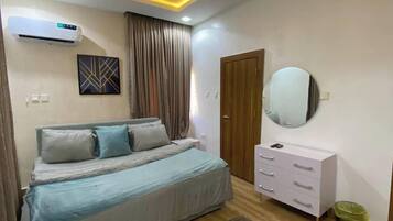 Un dormitorio con cama, cómoda, espejo, aire acondicionado y una alfombra estampada.