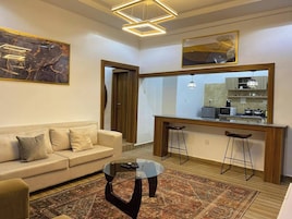 Uma sala de estar moderna com sofá, mesa de centro e área de cozinha com banquetas.