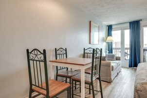 Una habitación con una mesa de madera y cuatro sillas, una cama, un sofá y un balcón con cortinas azules.
