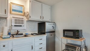 A compact kitchen with white cabinets, a stainless steel refrigerator, a microwave, and a toaster on a metal cart. - Beachfront Unit 17 Fall Escape by the Ocean! (Old Orchard Beach)