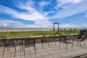 Un patio al aire libre con sillas y mesas de metal, con vista a una playa y el océano.