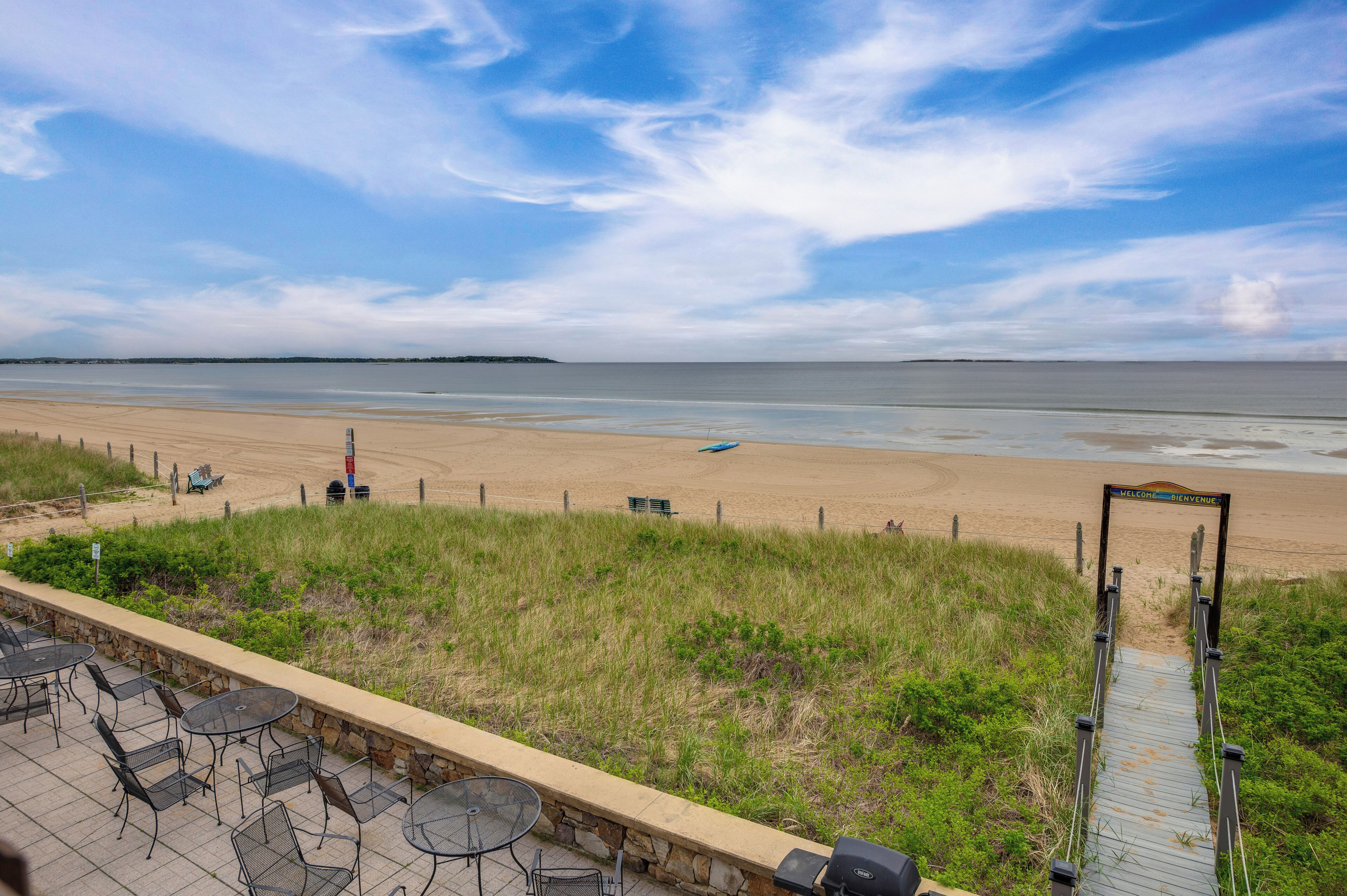 A beach view with a paved walkway leading to a sign reading "Welcome & Welcome".