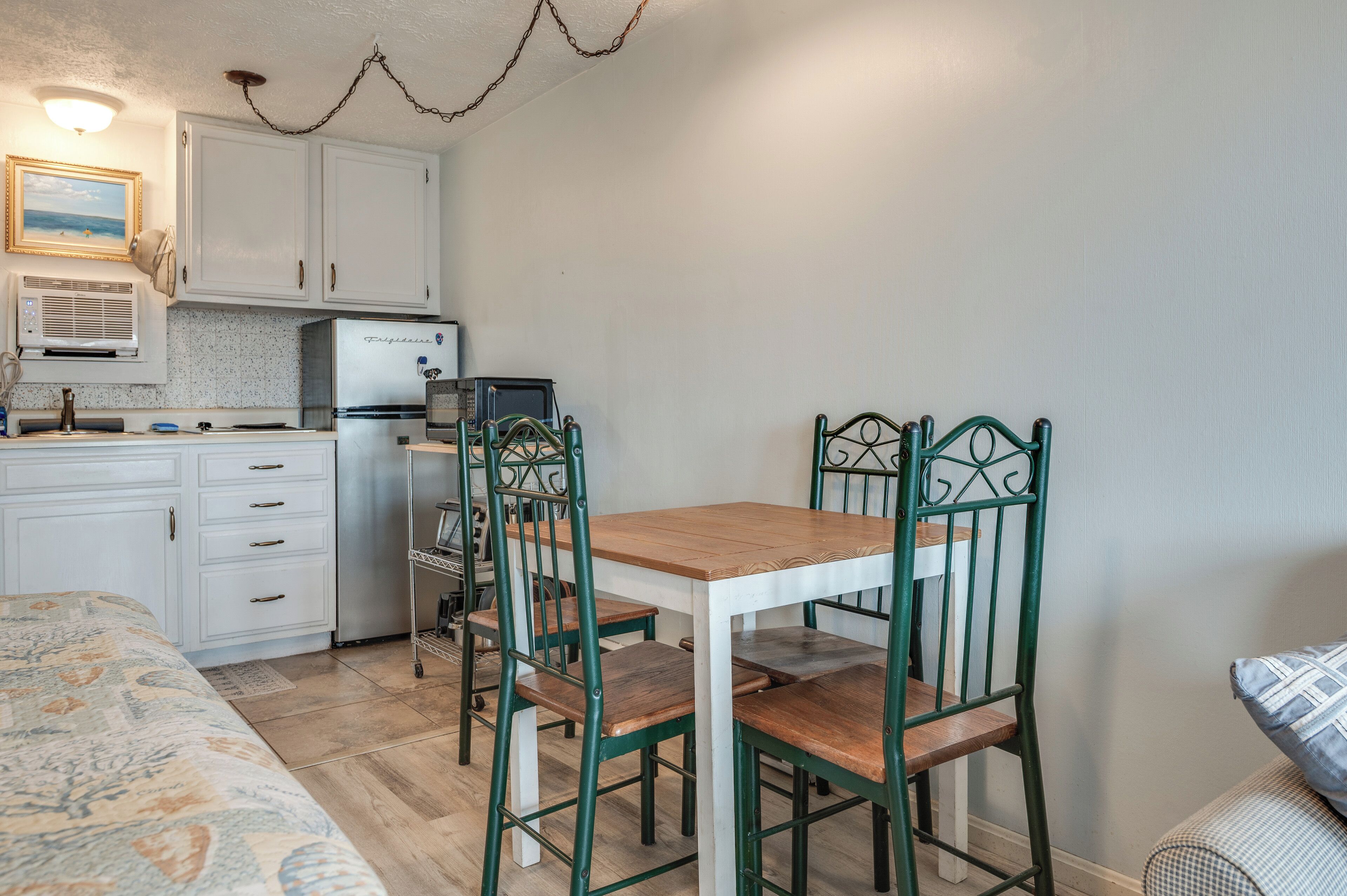 A compact kitchen with white cabinets, a microwave, and a refrigerator. There is a dining table with four chairs.