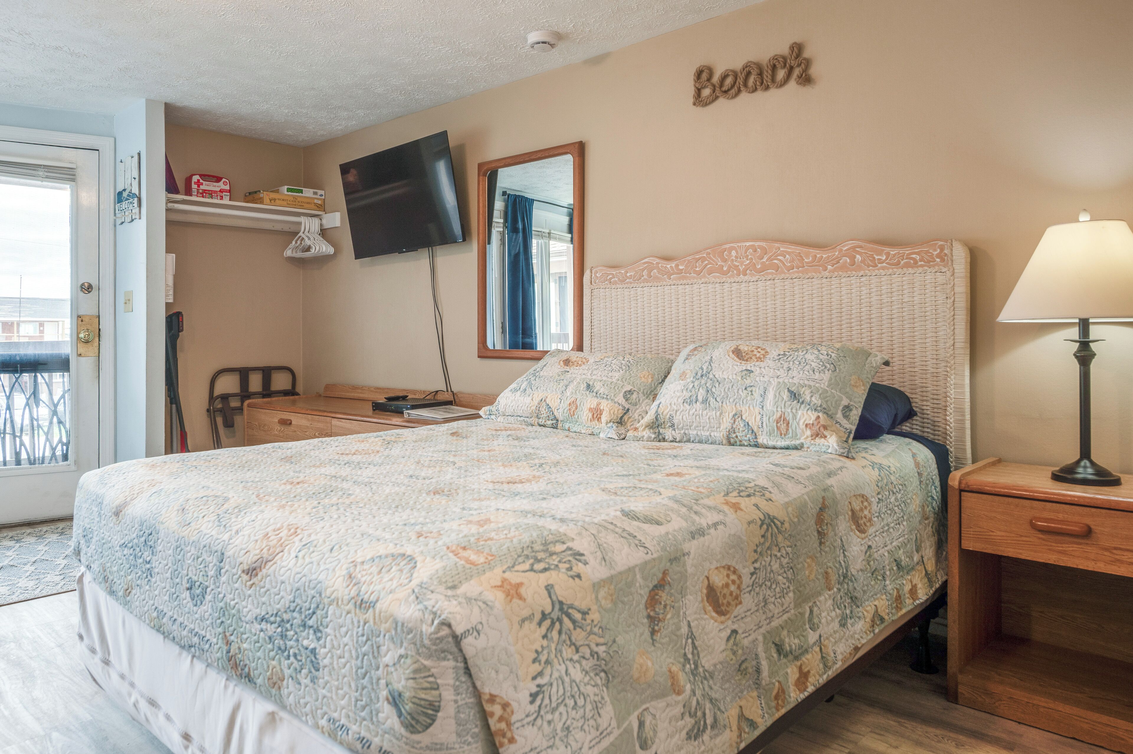 Un dormitorio con cama, mesita de noche, lámpara, televisor, espejo y estante con objetos.
