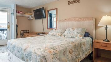 A bedroom with a bed, a bedside table, a lamp, a TV, a mirror, and a shelf with items.