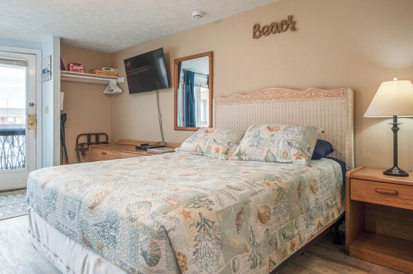 A bedroom with a bed, a bedside table, a lamp, a TV, a mirror, and a shelf with items.