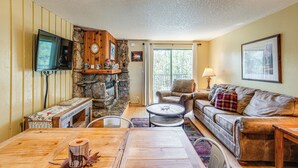 A cozy living room with a stone fireplace, a comfortable sofa, a wooden coffee table, and a television mounted on the wall. - 2 Mi to Winter Park Resort: Mtn-view Haven! (Winter Park)