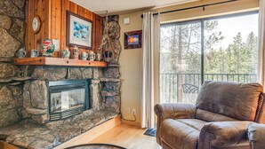 A cozy living room with a stone fireplace, leather sofa, and a large window offering a view of trees. - 2 Mi to Winter Park Resort: Mtn-view Haven! (Winter Park)