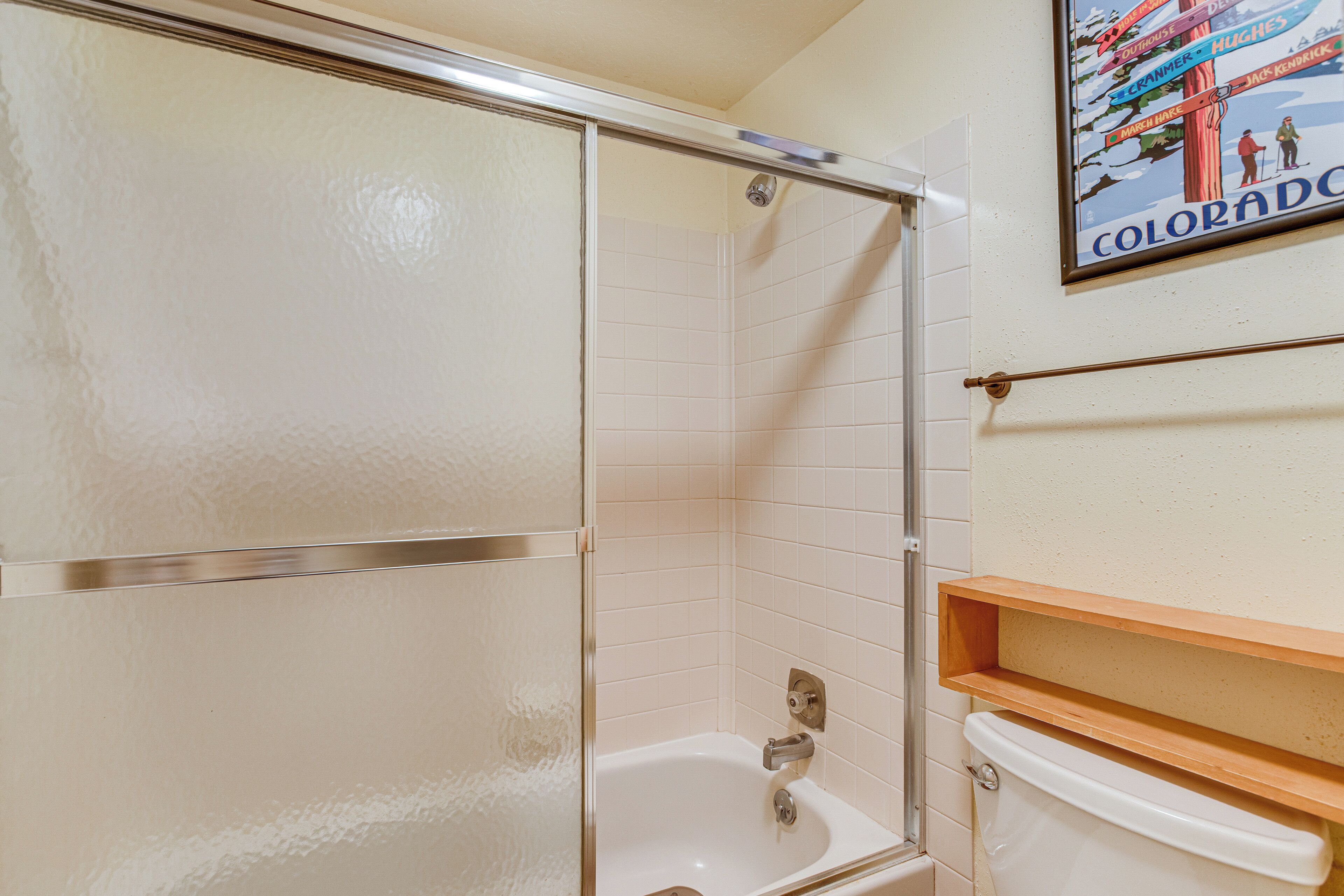 Un baño con cabina de ducha de vidrio, una bañera blanca y un estante de madera sobre la bañera.