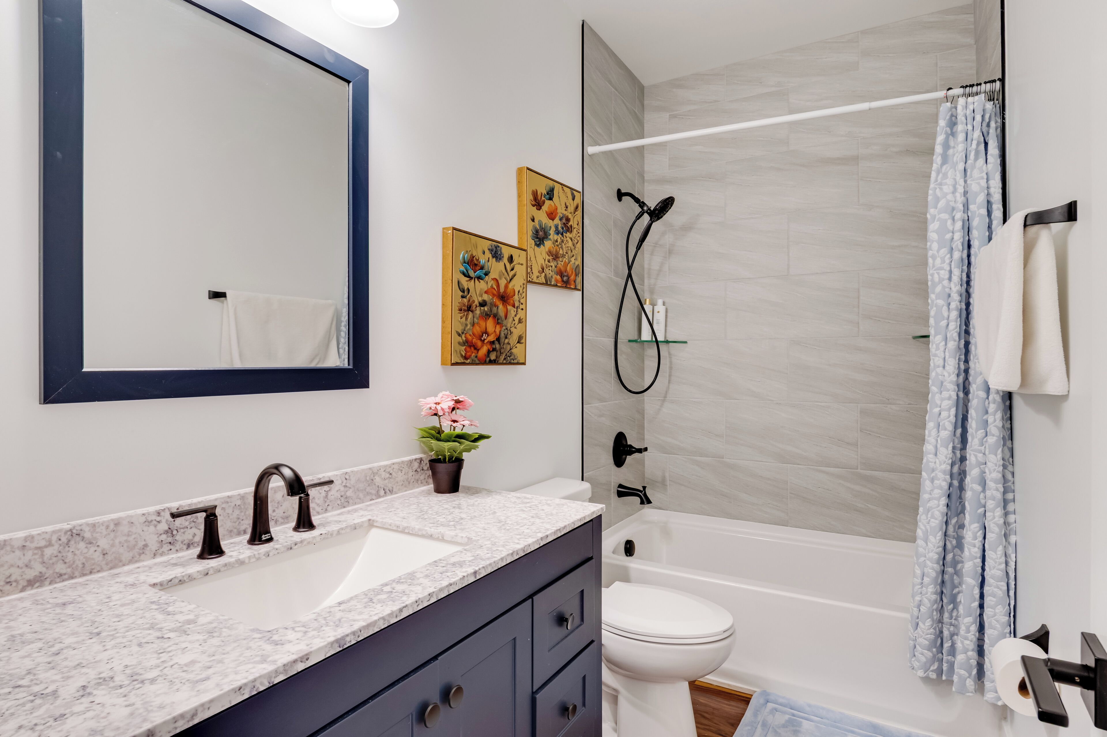 Een moderne badkamer met een marmeren wastafel, donkere kasten, een wit toilet en een douche met een glazen deur.