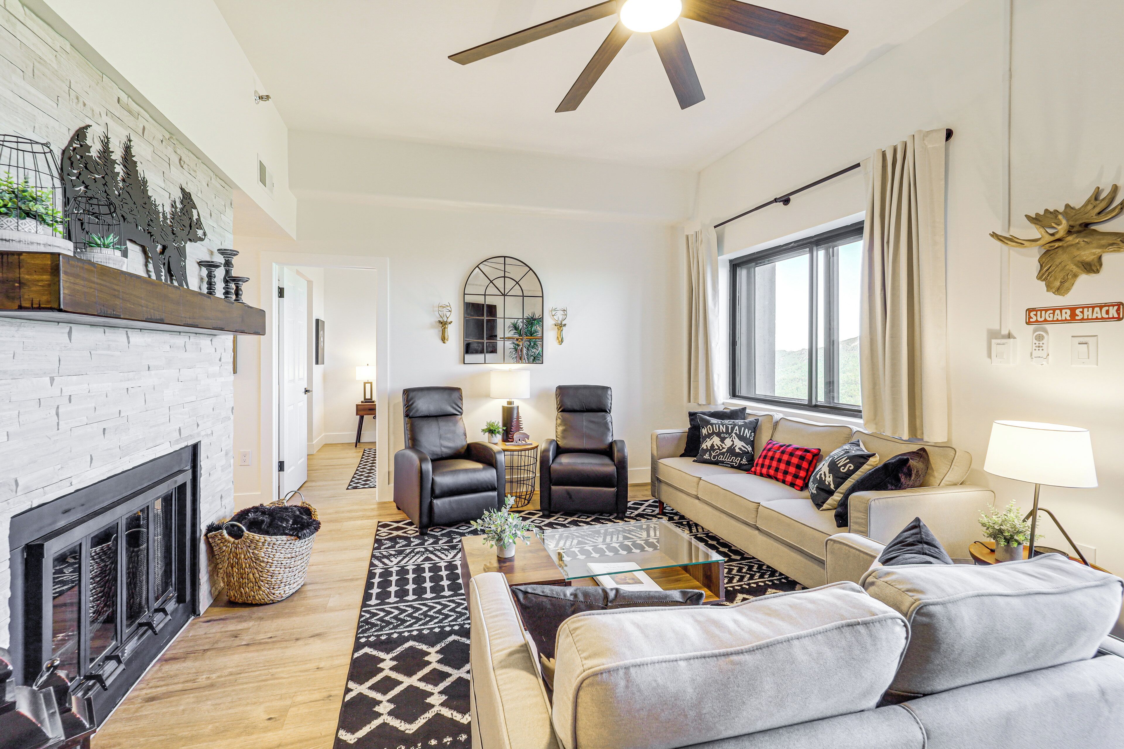 Un salon moderne avec une cheminée, des fauteuils en cuir, un canapé et une grande fenêtre.