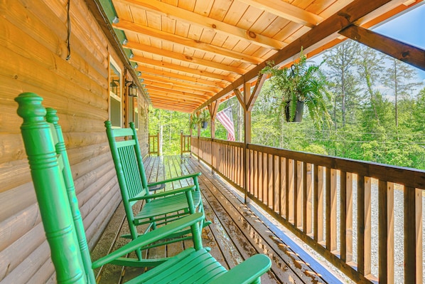 A wooden porch with green chairs and a railing overlooking a forested area. - Private + Secluded: Open-concept Sevierville Cabin (Sevierville)