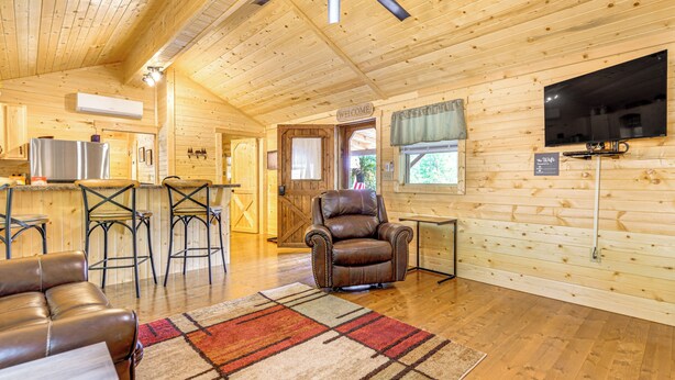 A wooden cabin interior with a living room, kitchen, and dining area.