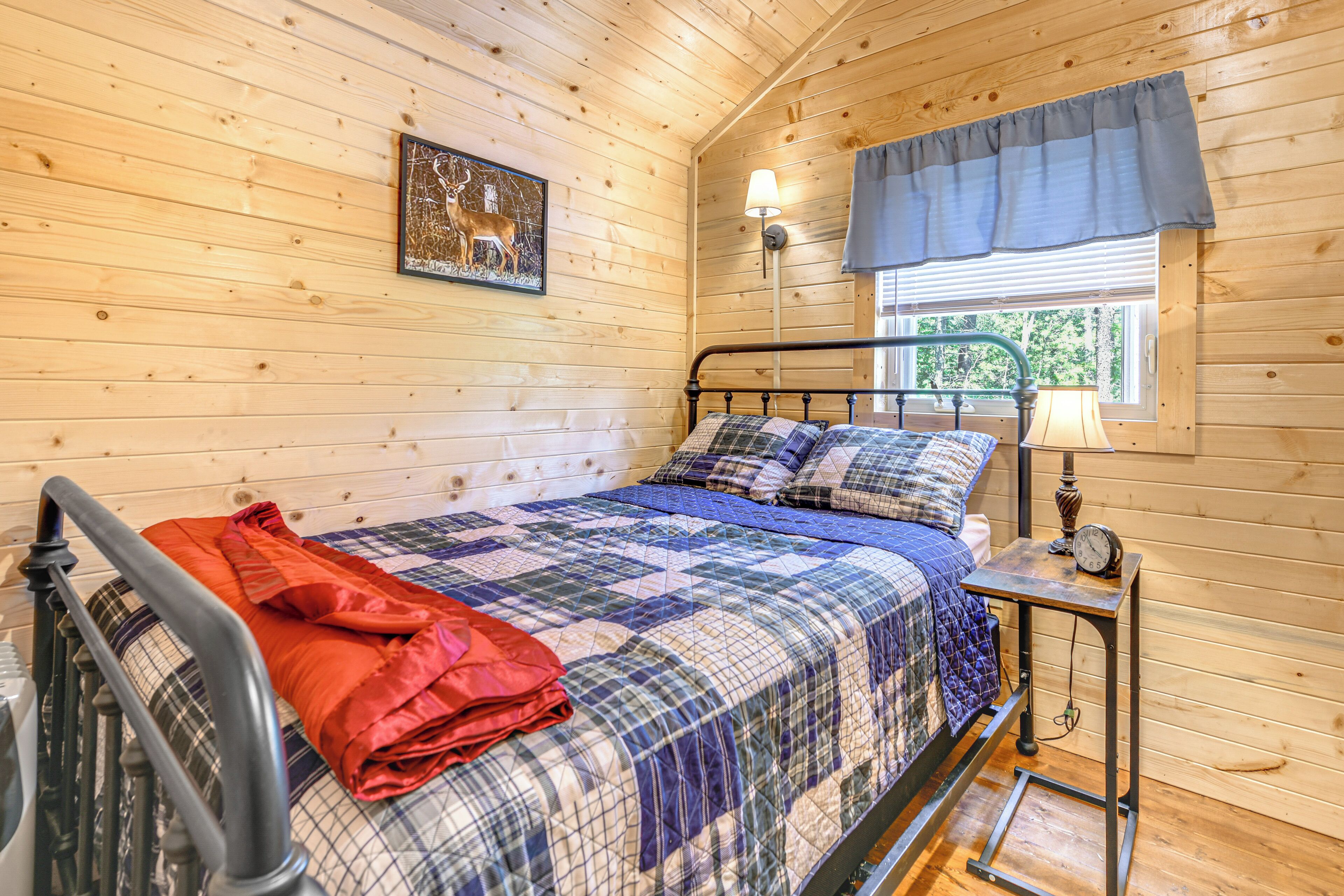 Une chambre à coucher dans un chalet en bois, avec un lit, une table de chevet, une lampe et une fenêtre avec des rideaux.