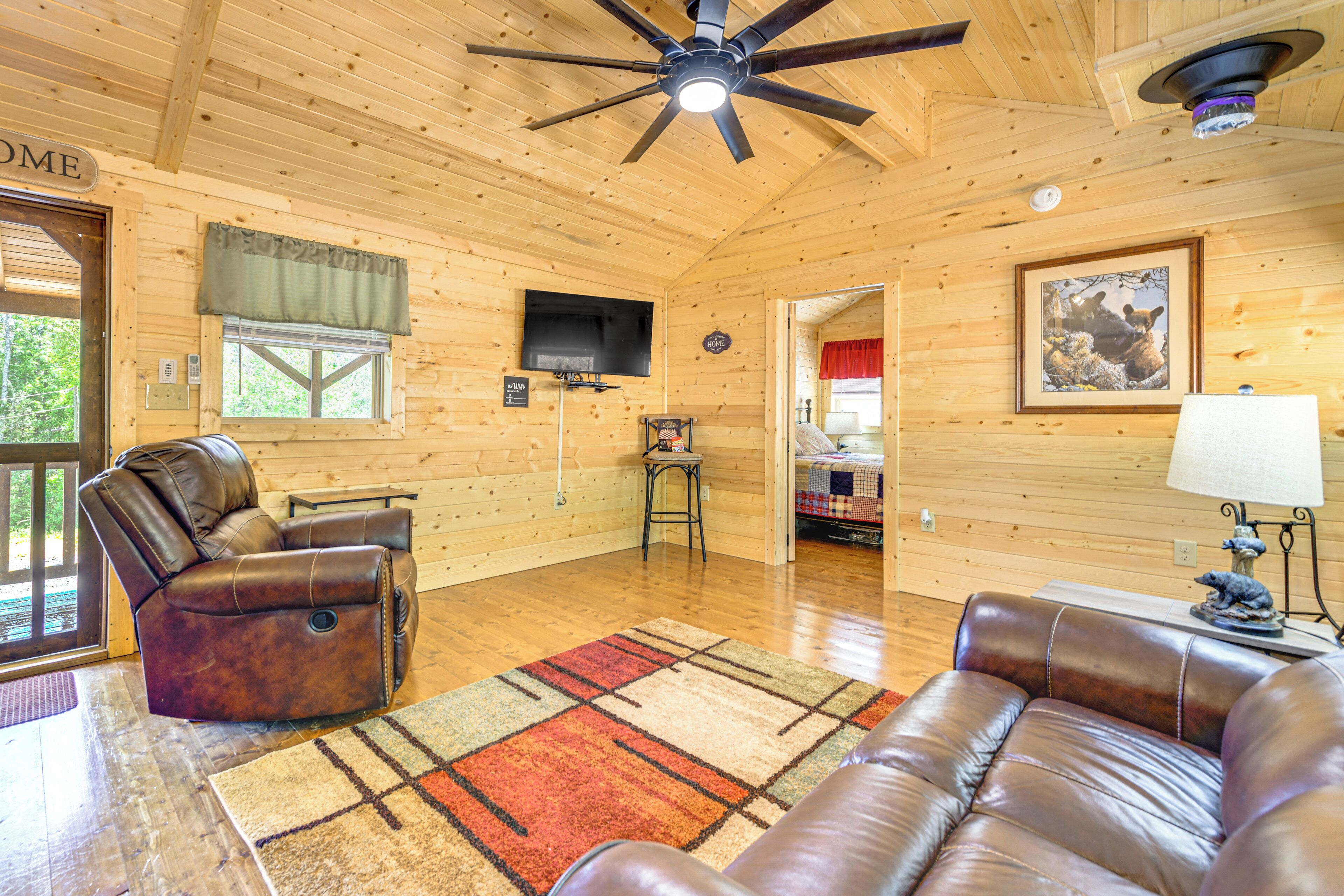 A cozy cabin interior with a leather recliner, a sofa, a TV, and a fireplace.