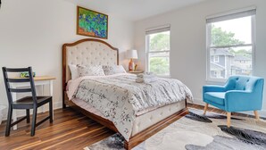 Een slaapkamer met een groot bed, een stoel, een bureau en een raam met uitzicht op huizen.