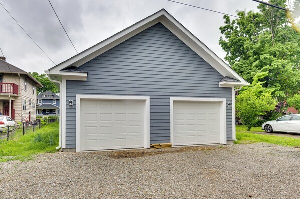 A two-car garage with a grey siding and white garage doors, set in a residential area with a gravel driveway and a red fence.