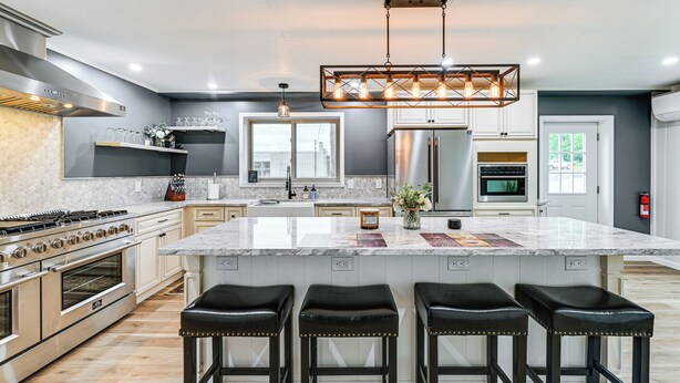 A modern kitchen with a large island, stainless steel appliances, and black bar stools.
