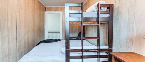 A bunk bed room with wooden walls, a white door, and a small wooden desk.