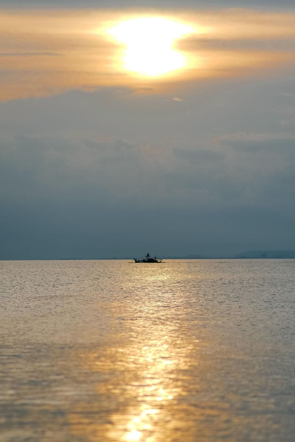 A calm sea with a boat in the distance and a bright sun near the horizon.