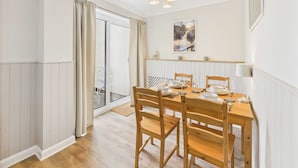 A dining area with a wooden table set for four, a chandelier, and a view of the outdoors through a sliding glass door. - Host Stay The Fairways (Stanley)