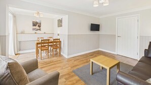 A modern living room with a wooden floor, a brown leather sofa, a wooden coffee table, and a dining area with wooden chairs and a table. - Host Stay The Fairways (Stanley)