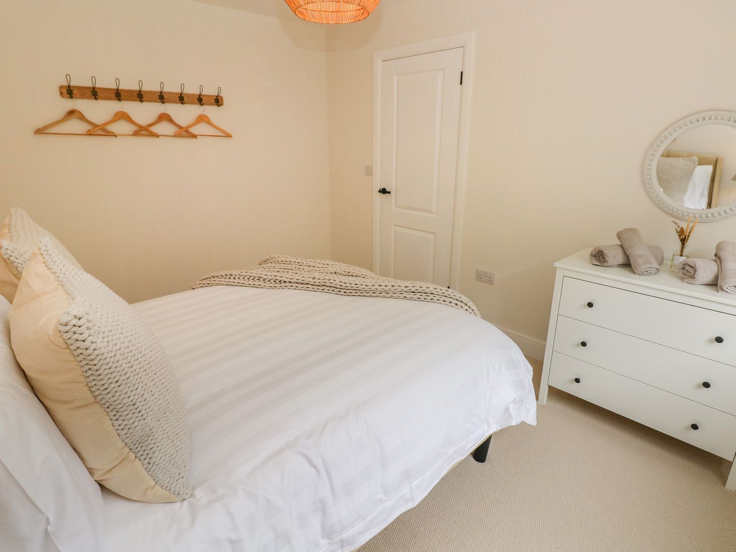 A bedroom with a bed, a dresser, a mirror, and a coat rack.