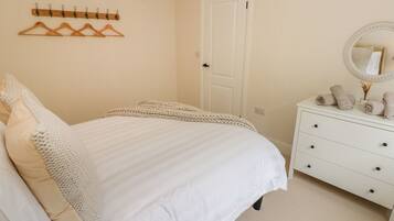A bedroom with a bed, a dresser, a mirror, and a coat rack.