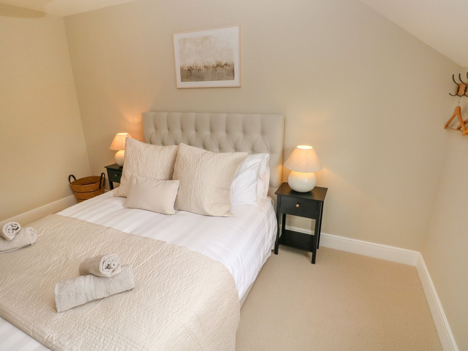 A neatly made bed with a beige headboard, two bedside lamps, and a framed picture on the wall.