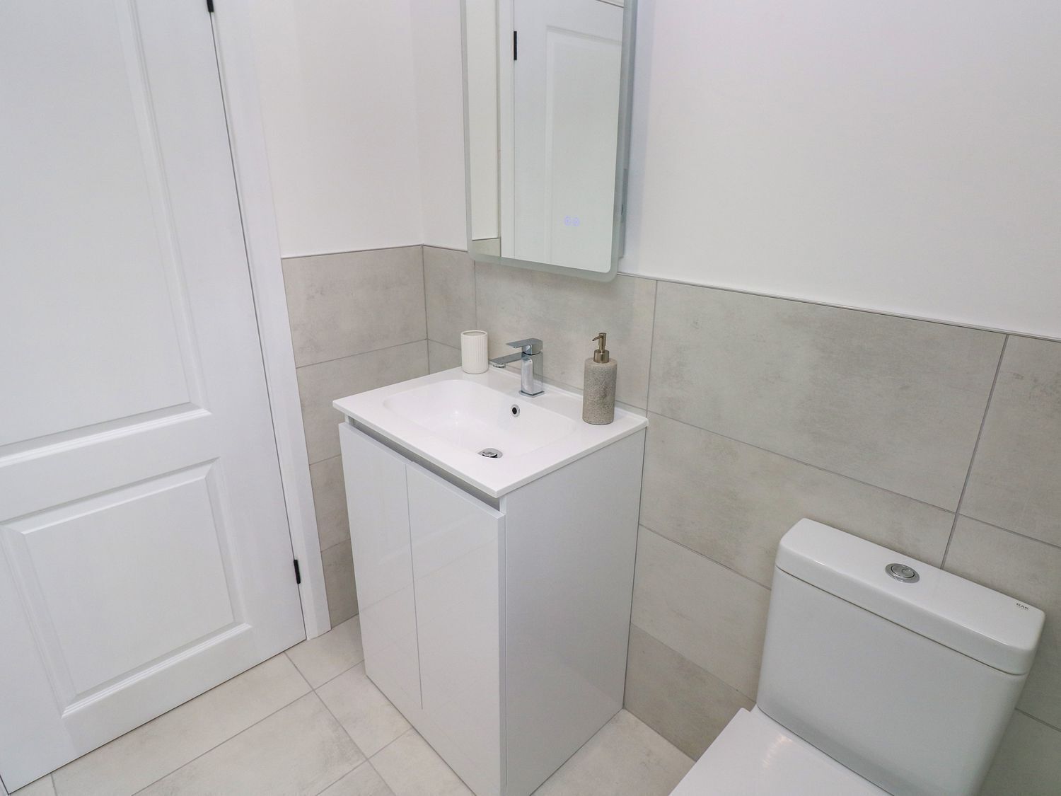 A bathroom with a white sink, a mirror, a toilet, and a cabinet.