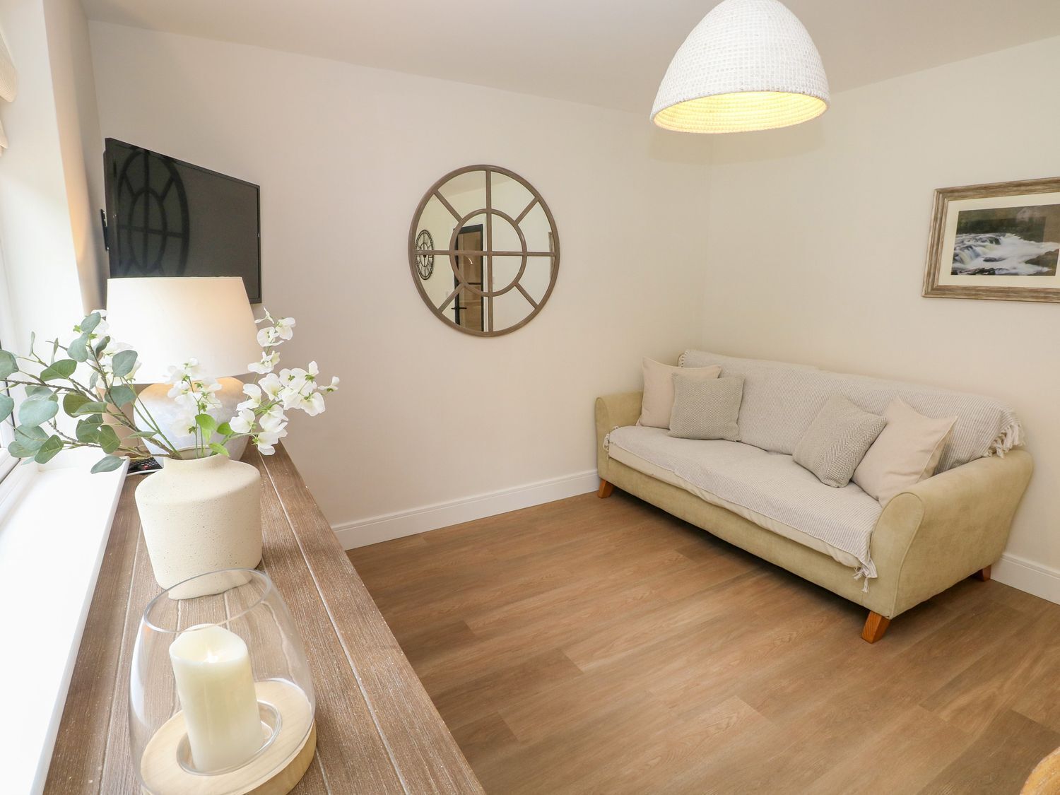 Un salón acogedor con un sofá color crema, un espejo redondo e iluminación colgante blanca.