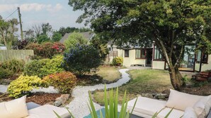 A garden with a seating area, a pathway, and a house in the background. - Candle Croft (Redruth)