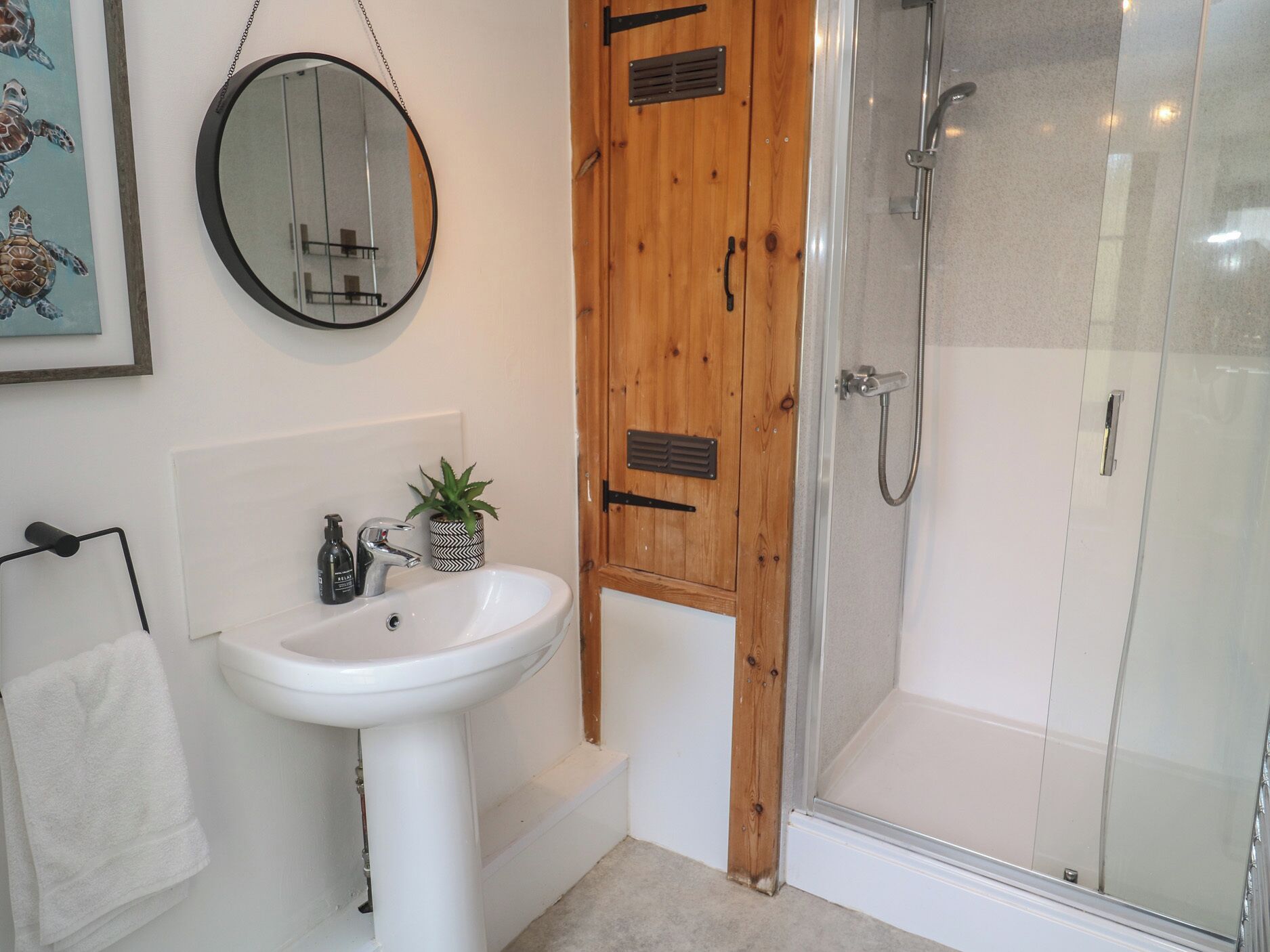 A bathroom with a white sink, a round mirror, a wooden door, and a glass shower enclosure.