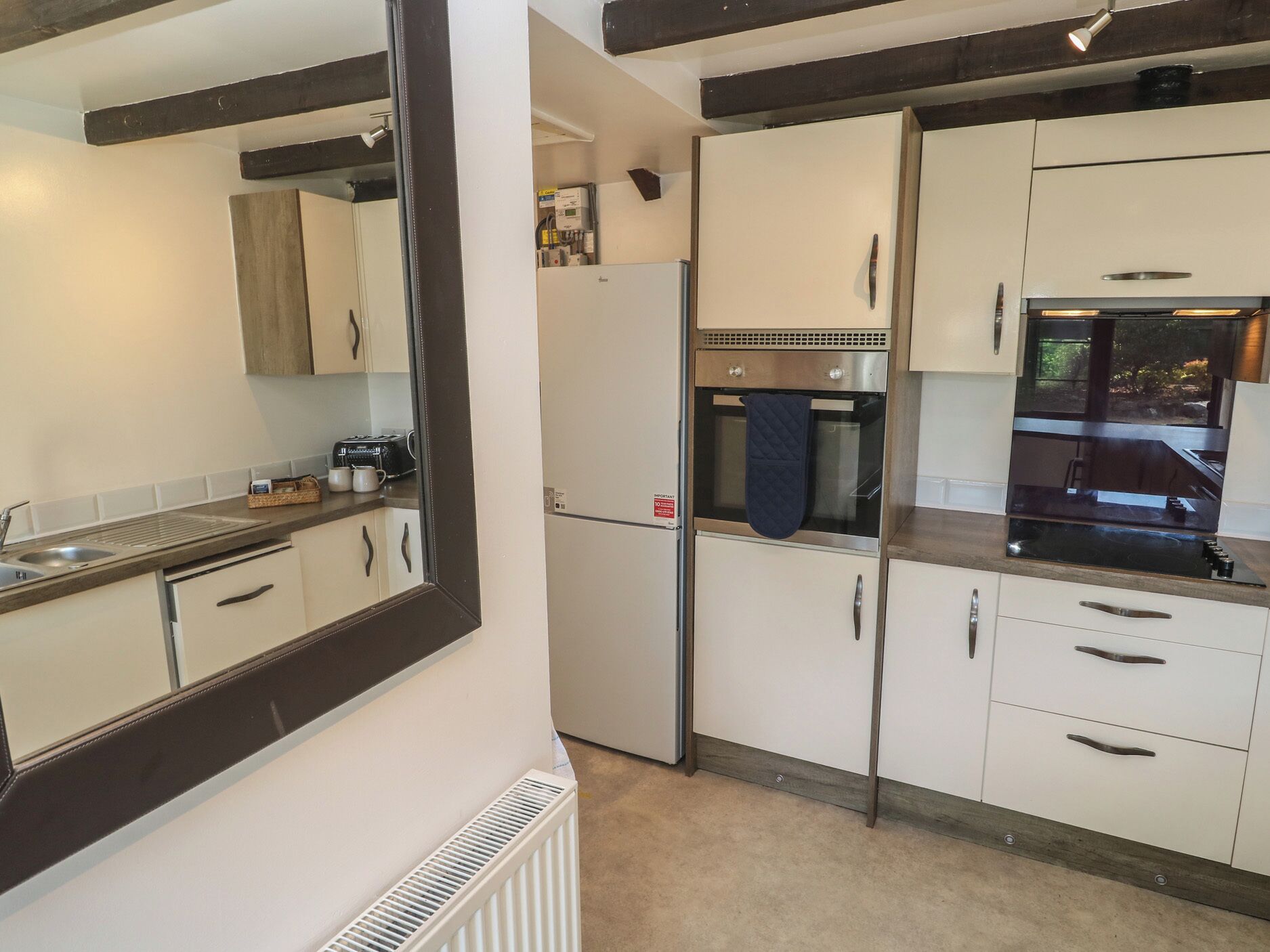 A modern kitchen with white cabinets, a stainless steel refrigerator, a built-in oven, and a large window.